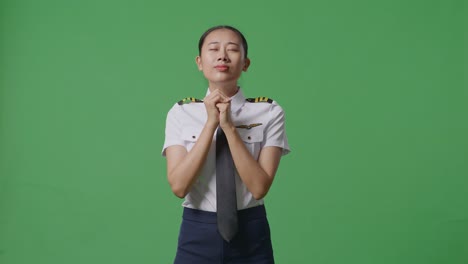 asian woman pilot praying for something while standing in the green screen background studio