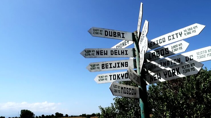 Cities distance arrow white signs against clear blue sky, low angle, circle pan