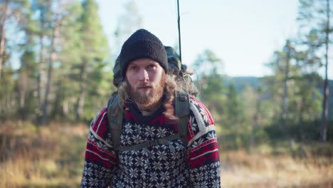 bearded man in beanie and sweater stop to rest during a hike in the forest