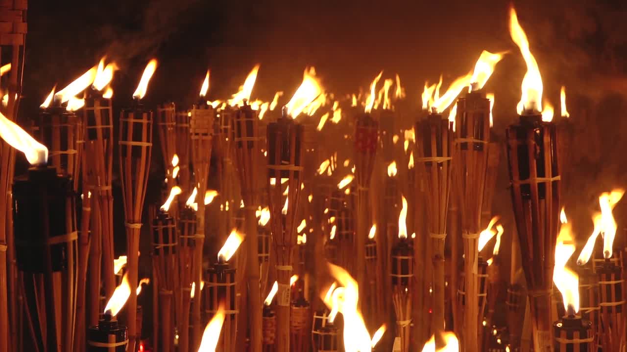 Close-up of a single lit bamboo torch with many others glowing in the blurred background, creating a warm and intense flame-filled atmosphere