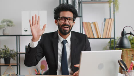 businessman working on laptop smiling friendly at camera and waving hands gesturing hello at office
