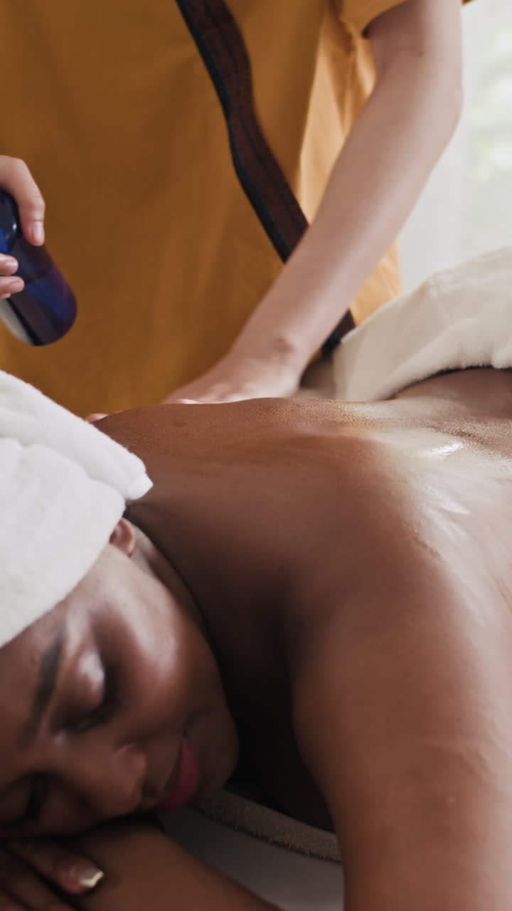 Massør smører lotion på ryggen af en kvindelig klient i en spa-salon