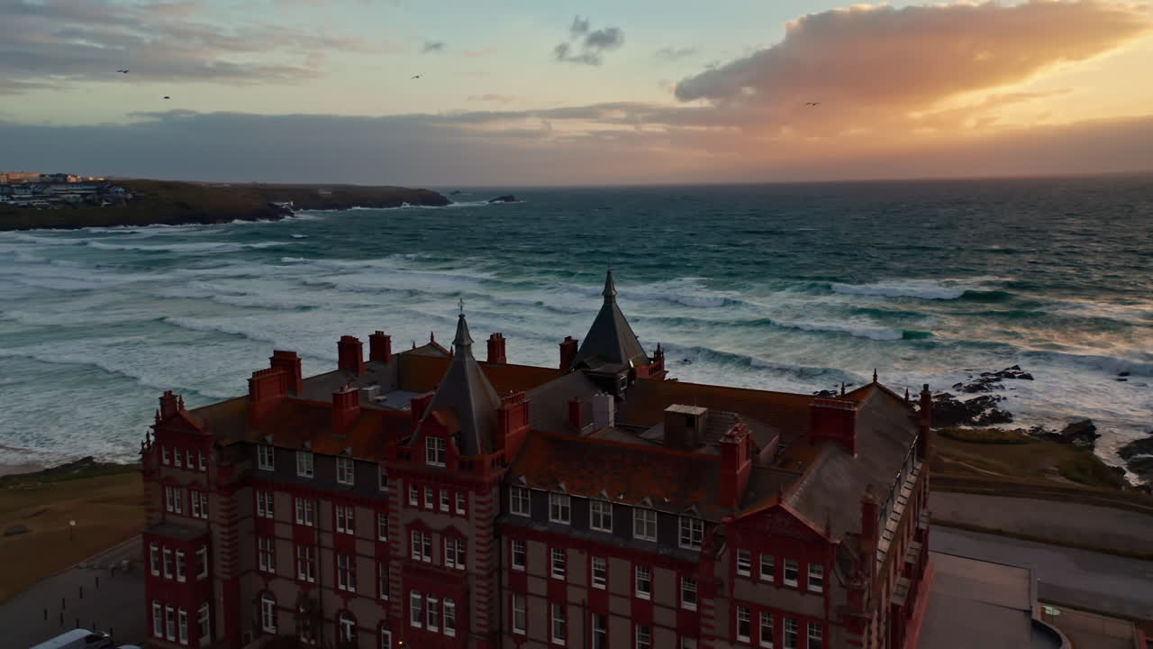 Aerial drone shot over the Headland hotel located on Cornwall's idyllic coastline.Sunset over the Cornish coastline, view of the sandy stretching beach, big waves coming to the shore.
