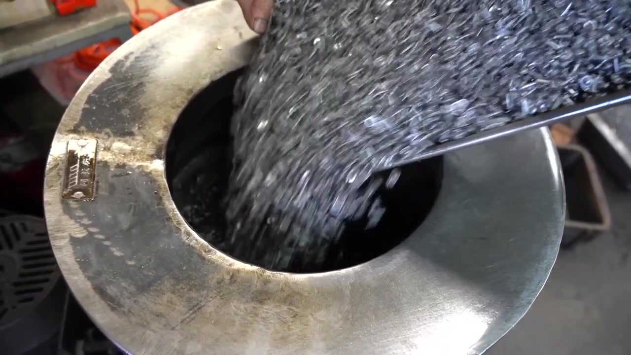 Trucioli di metallo grezzo che si riversano da un vassoio in una tramoggia rotonda che alimenta una macchina formatrice a vite