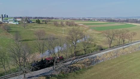 a vintage steam train chugs along tracks, alone, billowing smoke as it journeys through lush green fields and open countryside.