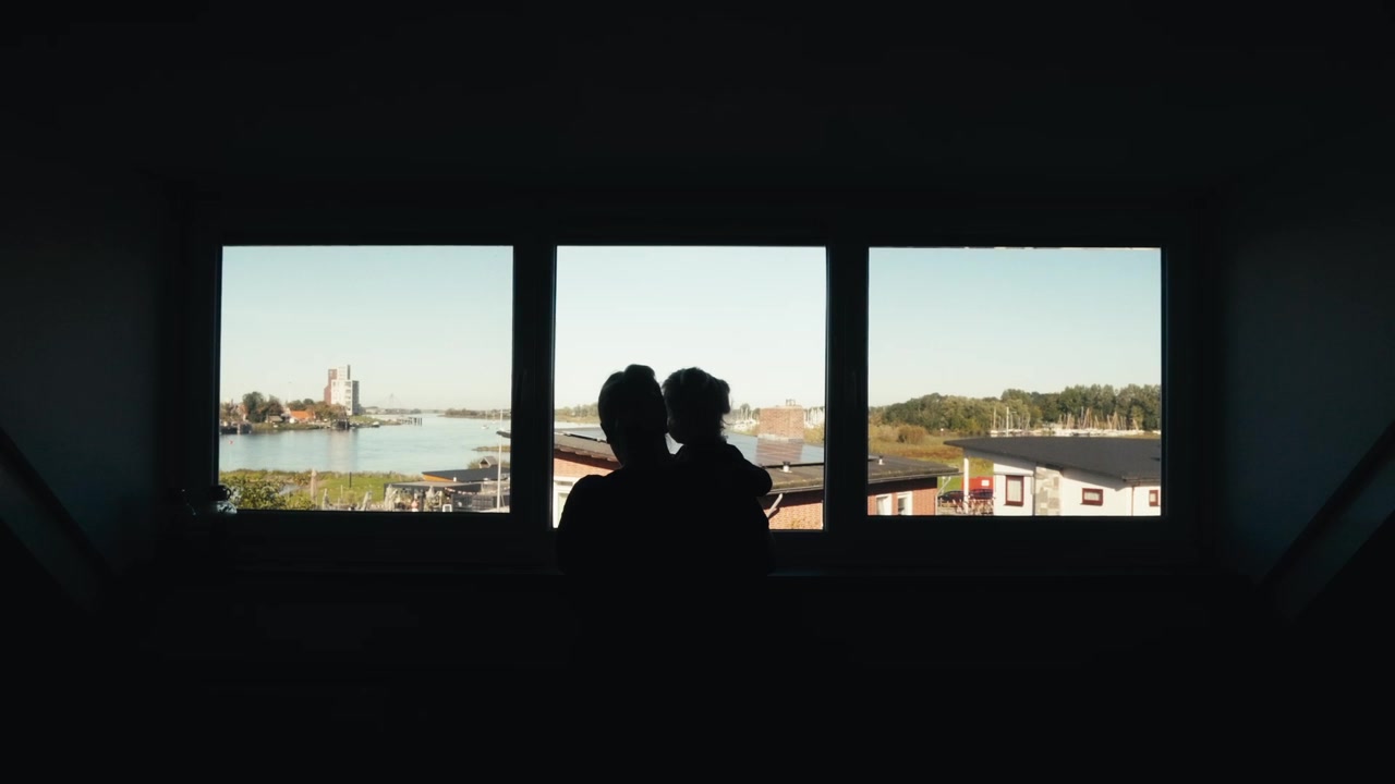 Cinematic Shot Mother With Child Looking At A River And The City, Through An Apartment Window In 4K.