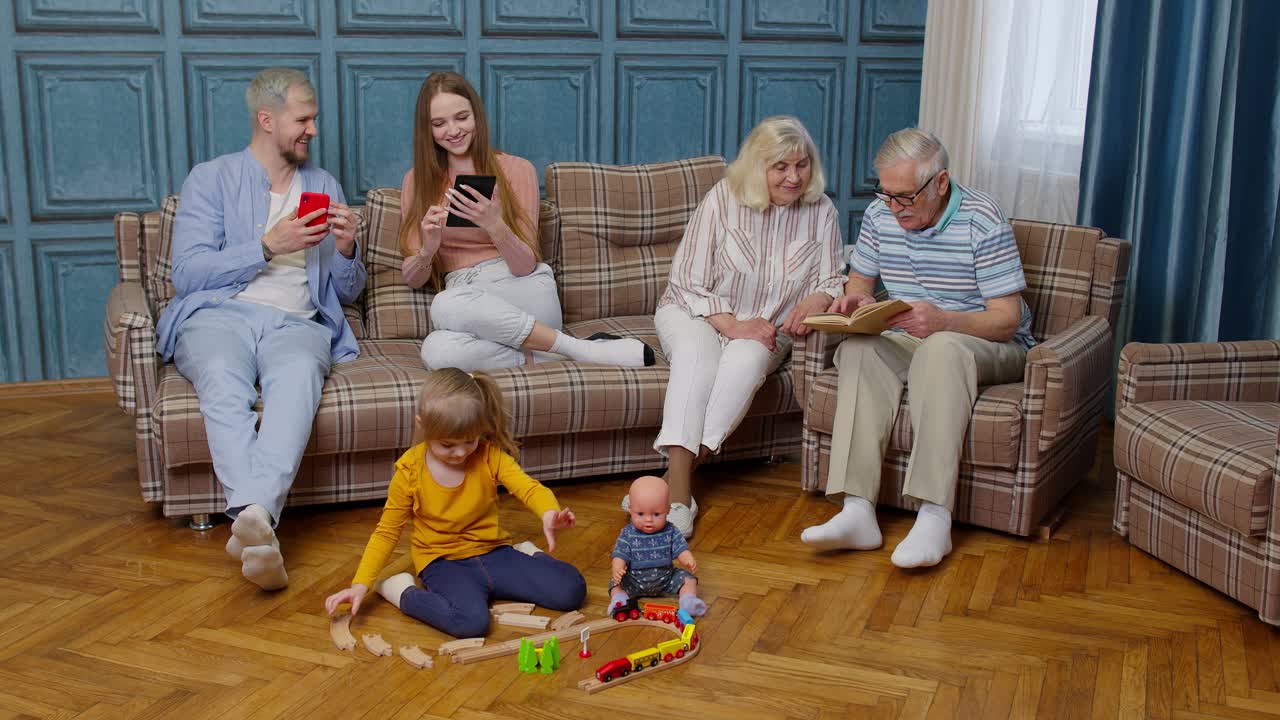 Multigenerational family leisure at home talking, reading book, use mobile phone, play game on sofa