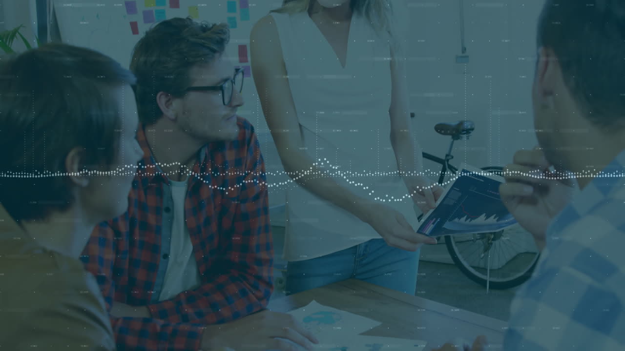 Coworkers sharing business data at desk, showing animated line chart on tablet, sticky notes