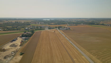 Hermoso-Paisaje-Agrícola-En-Kielno,-Polonia-Junto-A-La-Carretera-Con-Tractores-Cosechando-En-Un-Clima-Cálido-Y-Soleado---Disparo-De-Drone-Descendente