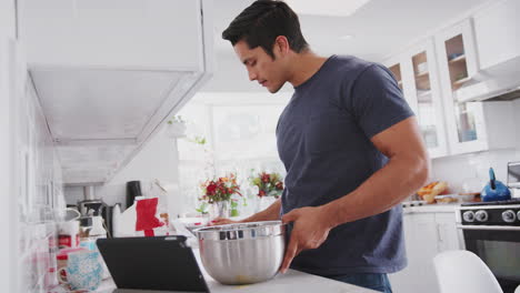 Millennial-man-preparing-cake-mix-following-a-recipe-on-a-tablet-computer,-adding-milk,-close-up