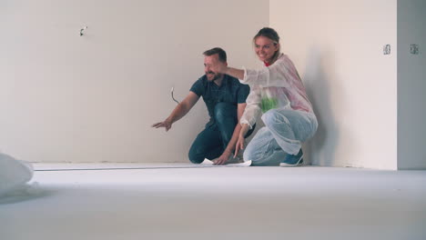 una hermosa pareja desenrolla el papel pintado abrazándose en el suelo de la habitación