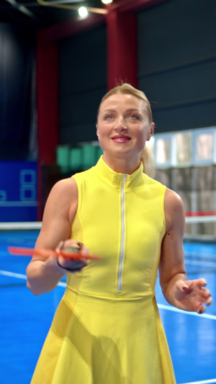 Woman in a yellow dress training to play pickleball on a blue, inside court. Vertical