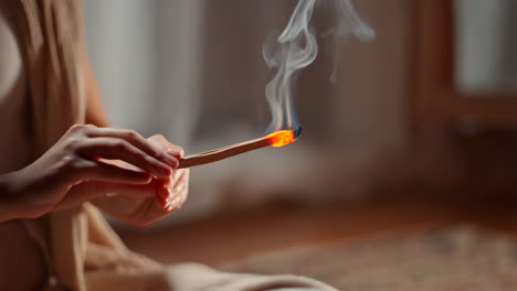hands holding burning palo santo stick with rising smoke