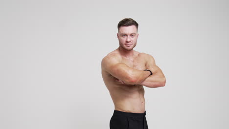 caucasian man standing his back to camera turns around to camera. athlete with naked torso crosses hands on his chest looking at camera. white backdrop.