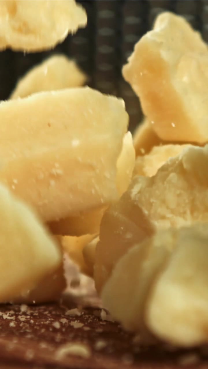 Scaglie di Parmigiano che cadono al rallentatore su un tagliere di legno