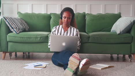 young african american woman tutor with laptop sits on floor in apartment