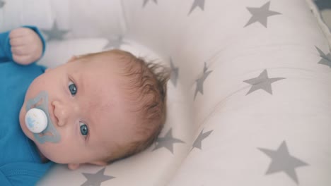 cute-boy-with-large-blue-eyes-sucks-pacifier-in-soft-cocoon