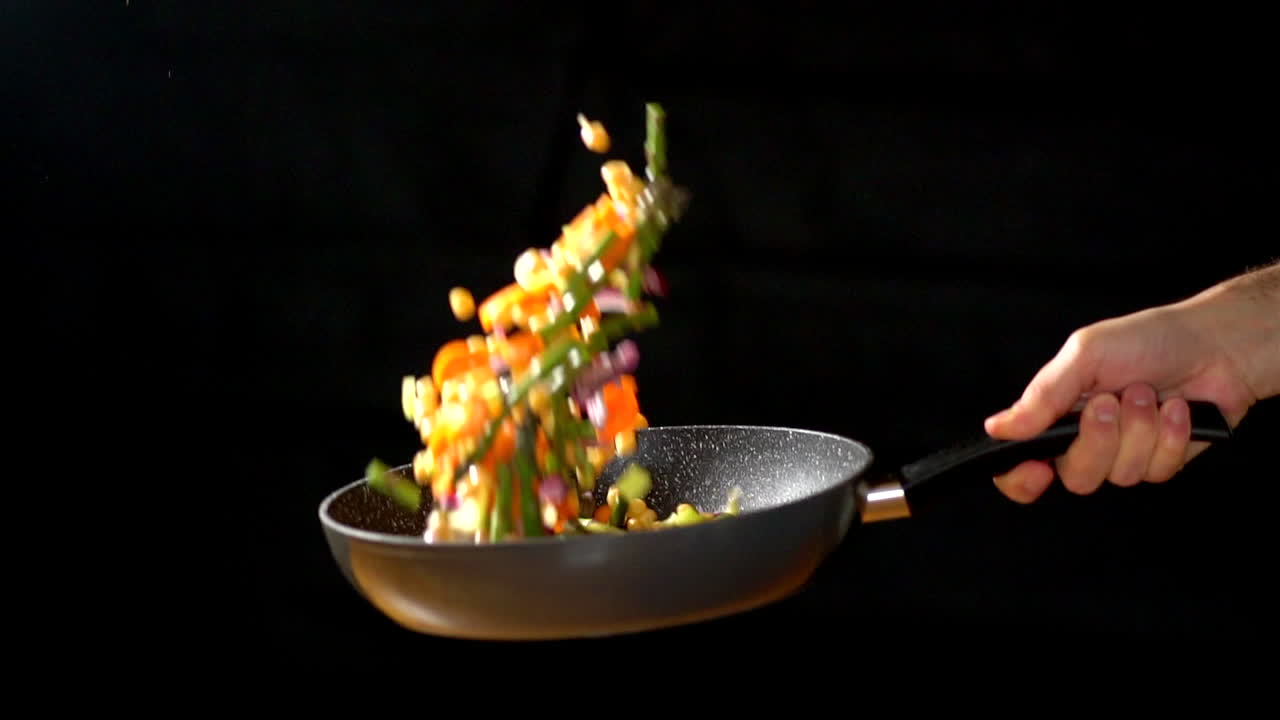 cu slowmotion: chef che tiene il wok mentre lancia le verdure in un'illuminazione da studio