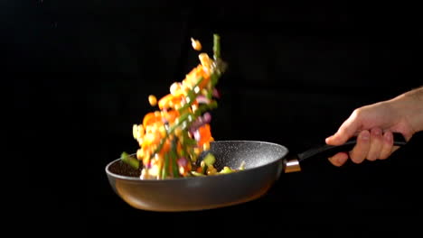 cu slowmotion: chef holding wok while tossing vegetables in a studio lighting