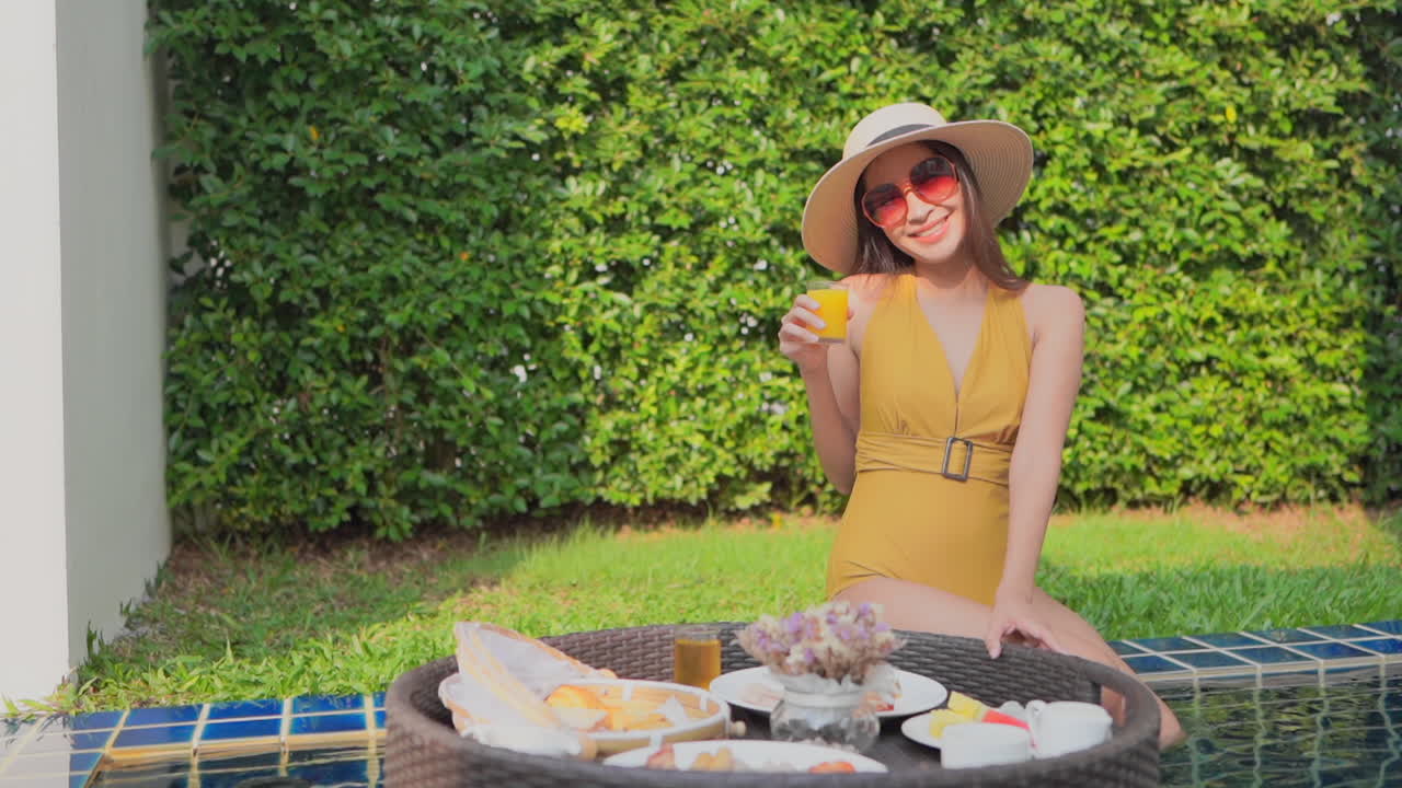 Woman sits on edge pool with big floating tray full of drinks and food