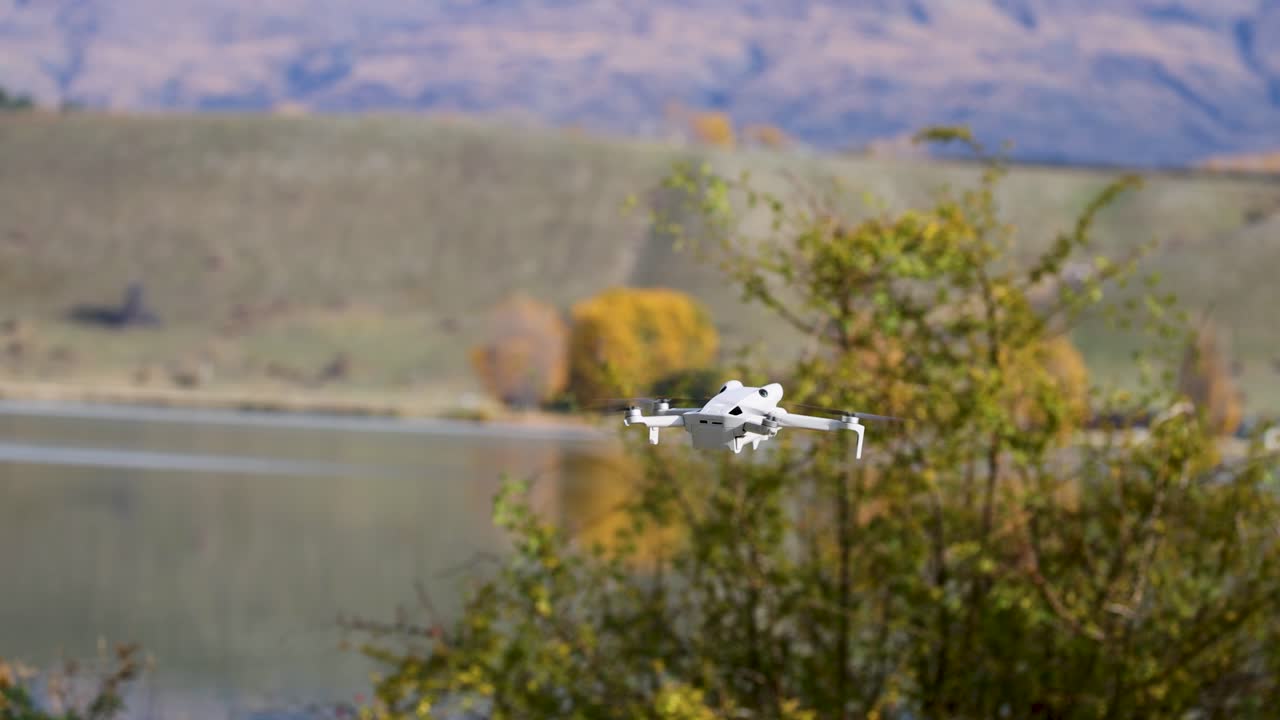 A drone navigates through a picturesque New Zealand landscape with mountains and autumn foliage, captured in smooth motion