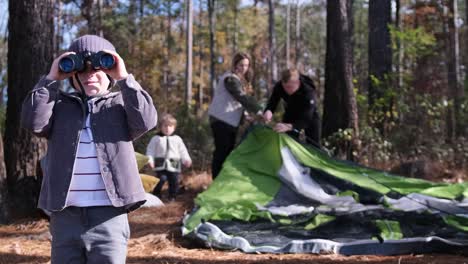 a family enjoys a woodland adventure setting up a tent and exploring in a serene woodland a family enjoys an outdoor adventure a boy uses binoculars to admire nature while his family sets up a tent emphasizing fun and family bonding
