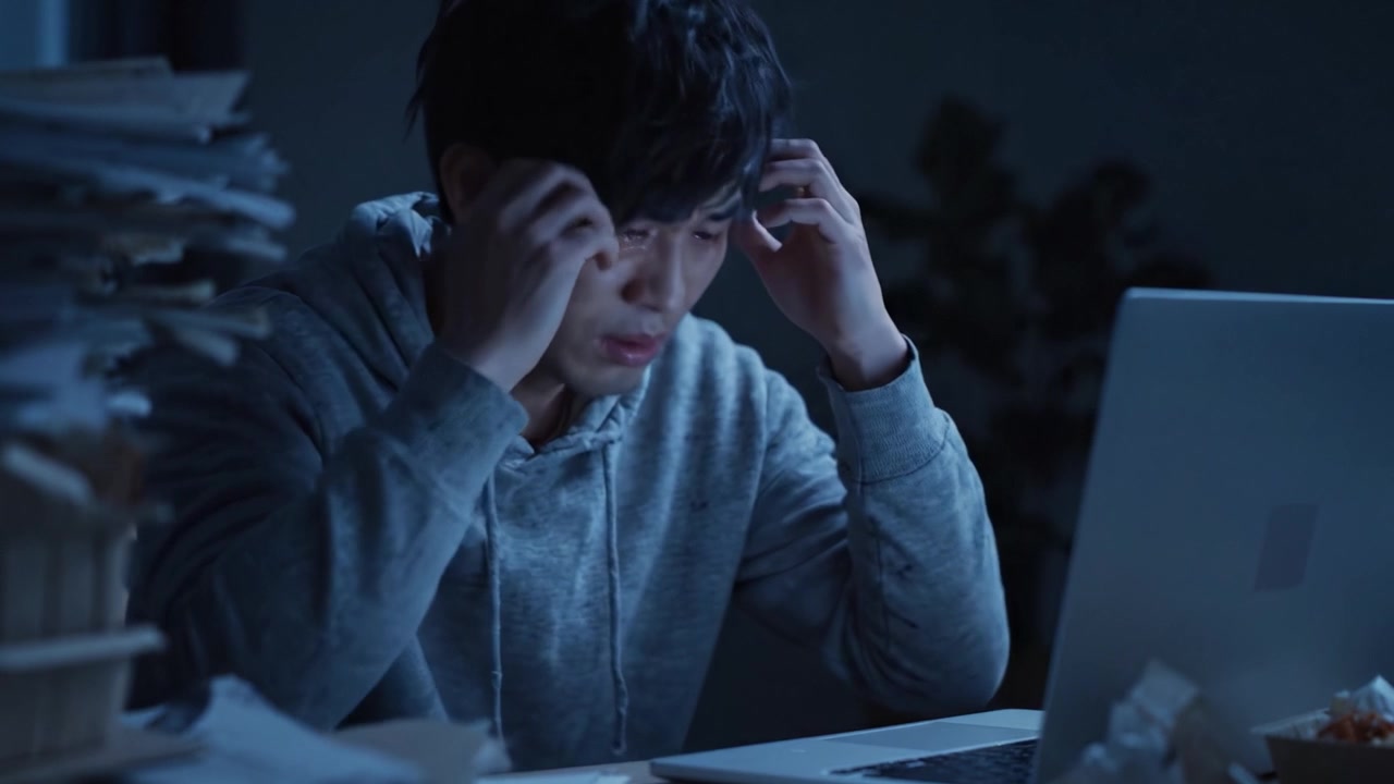 A Focused Man Battles Exhaustion Late at Night, Engaged with His Laptop in an Overwhelming Environment Filled with Paperwork and Shadows