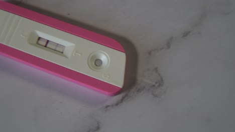 toma deslizante de una prueba de embarazo rosa positiva en la mesa de mármol