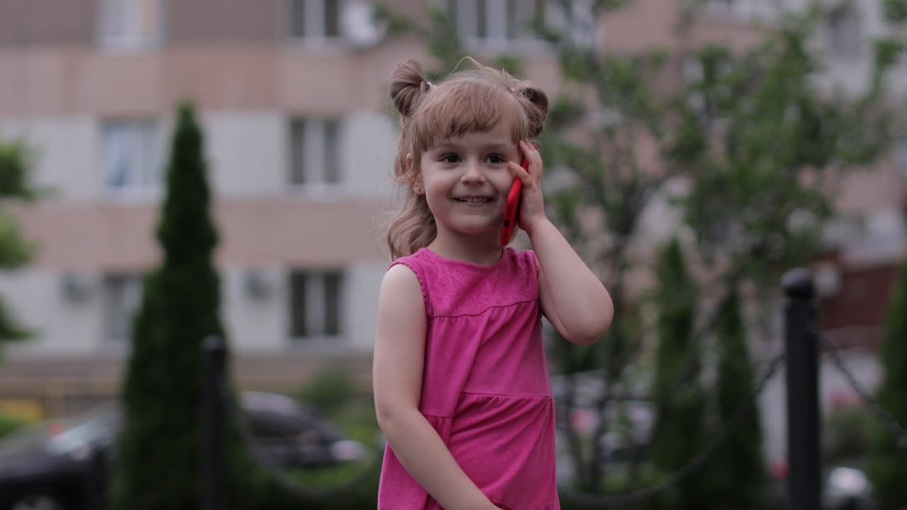niña hablando por teléfono inteligente al aire libre. niño con vestido rosa hablando por teléfono móvil en la calle de la ciudad