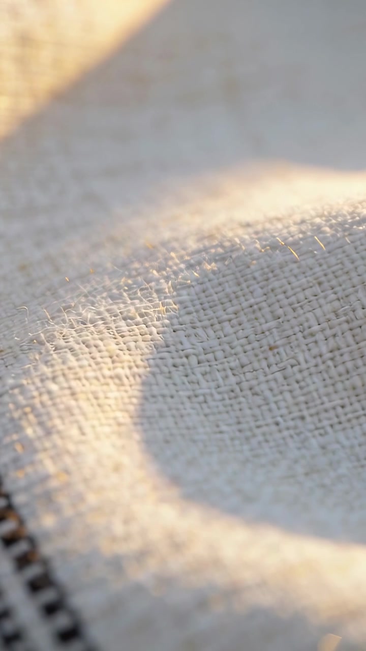 Video verticale: Luce calda che si sposta, ombra ad anello che svanisce su tessuto beige dopo l'inclinazione, cerniera nera.
