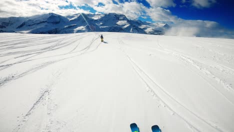 skiing in powder with a person skiing in front with mountains as a backdrop