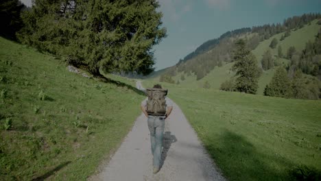 Gimbal-tracking-backpacker-in-casual-clothing-hiking-on-rural-dirt-road-in-mountain-valley