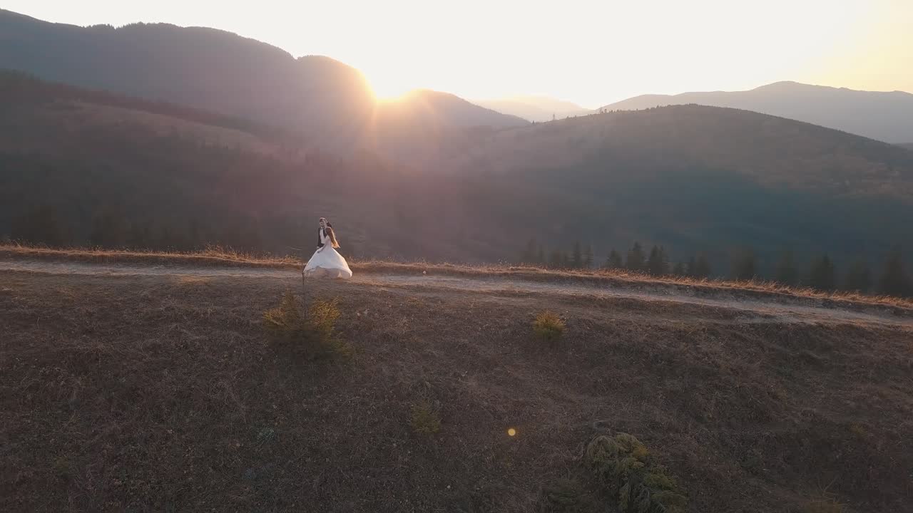 la novia y el novio posan en la cima de la montaña al atardecer