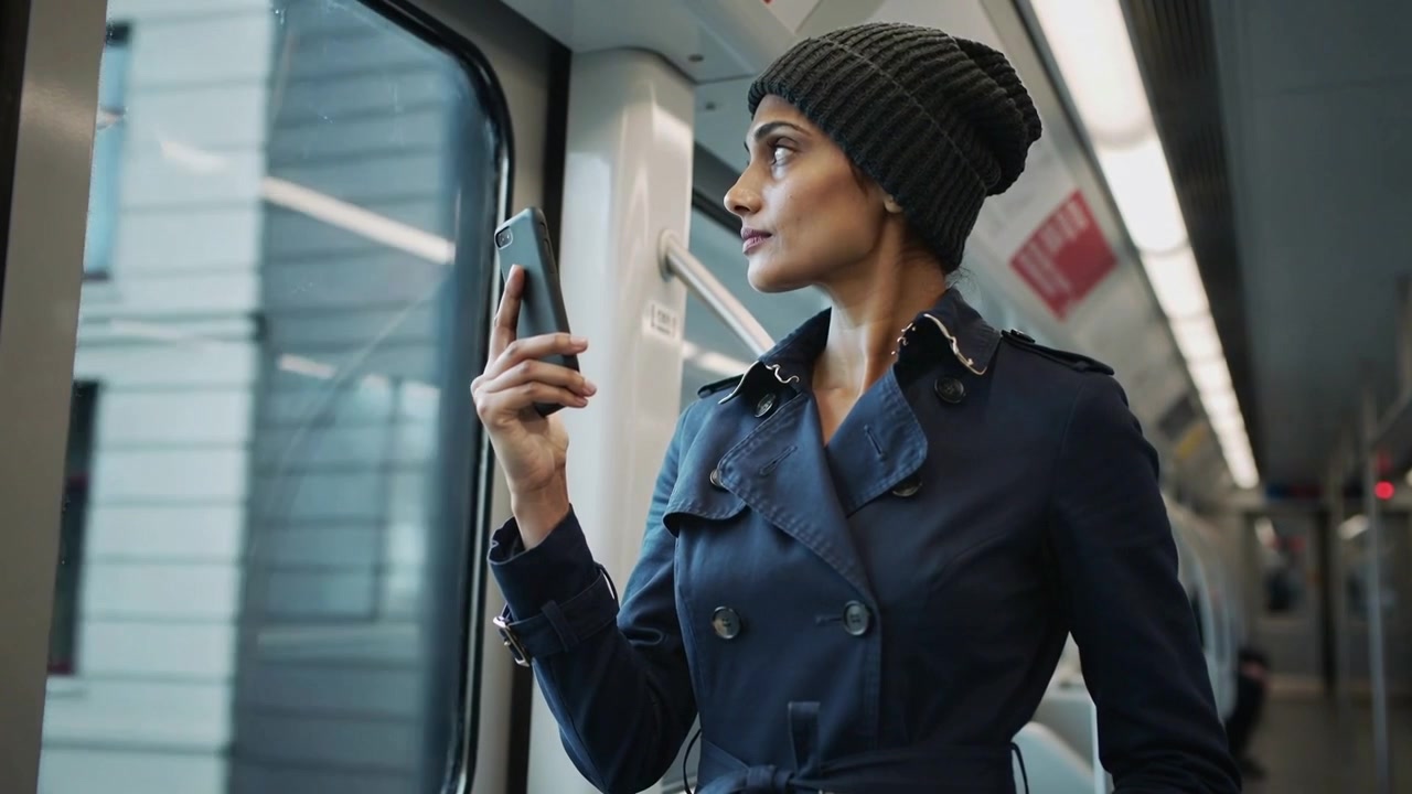 Reacting to tram movement, woman wearing navy trench coat holding phone and gazing through window