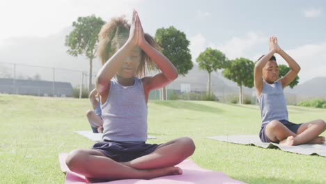 Video-of-three-african-american-schoolchildren-practicing-meditation-in-outdoor-class