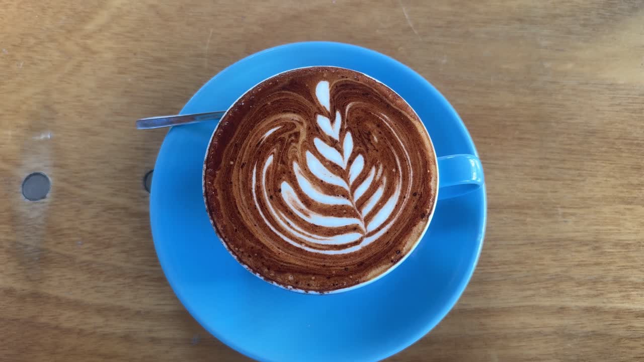 Cappuccino coffee latte art, blue mug caffeine drink with milk, wooden table artisan shop