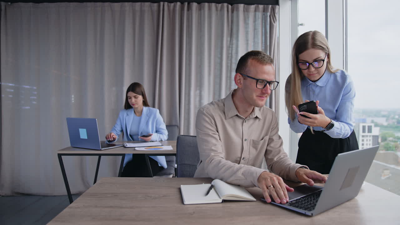 Busy people working in the modern office. Company employees solving job issues. Lady with phone standing at man in front of computer. Brunette woman at desk at backdrop.