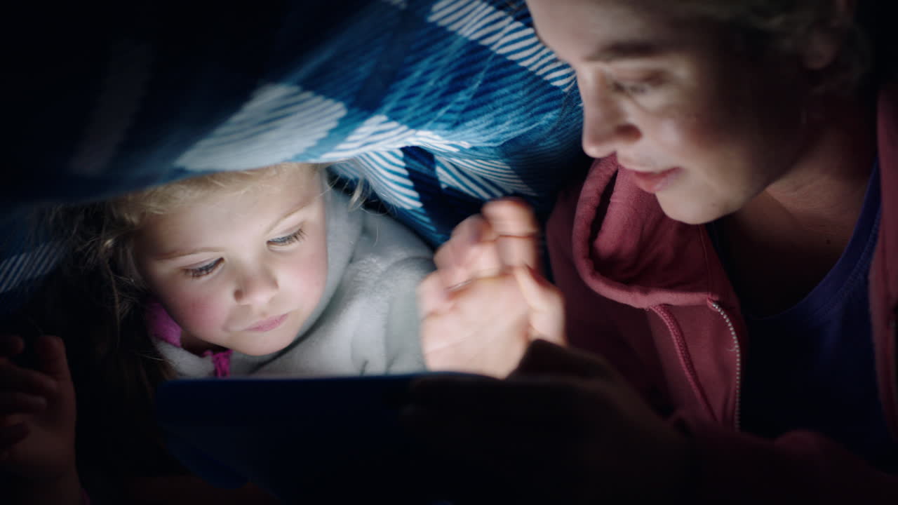 madre e hija felices usando una tableta bajo una manta jugando juegos en la tecnología de pantalla táctil relajándose divirtiéndose antes de acostarse