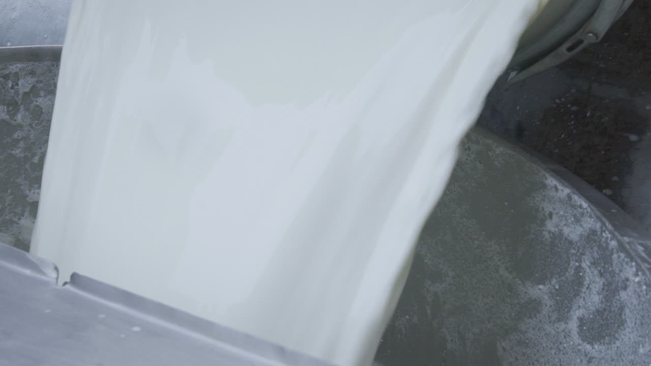 una vista de cerca del llenado de leche en un recipiente por un tambor blanco, el hombre llevaba guantes de plástico en las manos, cámara lenta