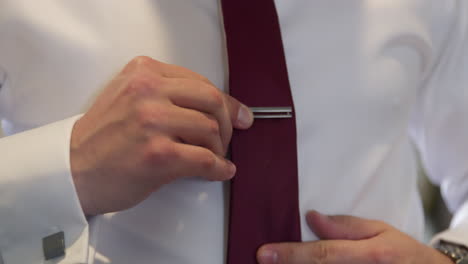 latin groom in white shirt adjusting his red tie with a metallic bar clip