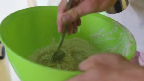 mixing flour with water using a spoon in a green bowl to make a dough for baking