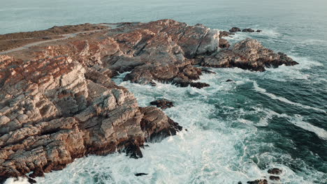 Olas-De-Mar-Espumosas-Salpicando-En-La-Costa-Rocosa-Durante-El-Verano-En-Vleesbaai,-Cabo-Occidental,-Sudáfrica---Toma-Aérea-De-Drones