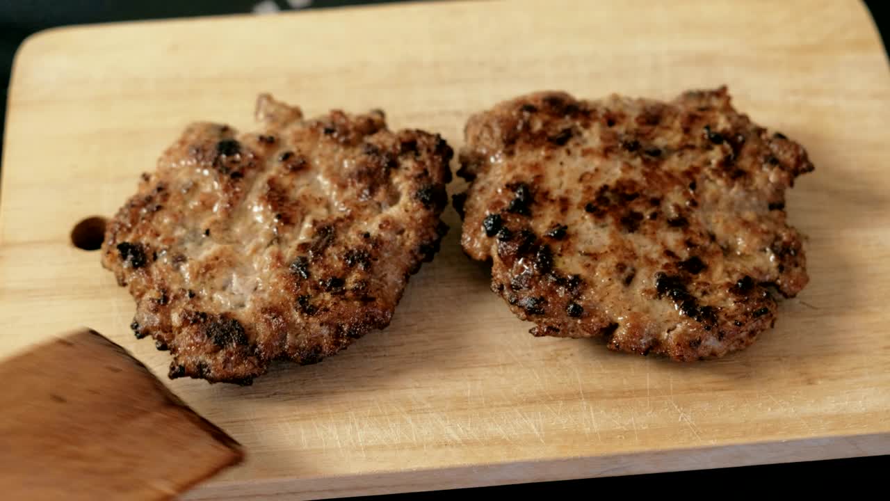 Putting cutlets for burgers on wood board with wooden spatula.