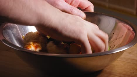 hand is mixing vegetables in a metal bowl, roasted vegetables with fried chicken