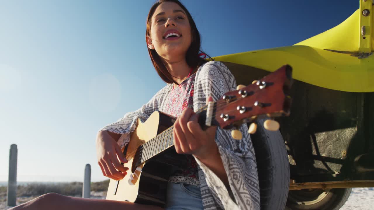 feliz mujer caucásica sentada en un buggy de playa junto al mar tocando la guitarra