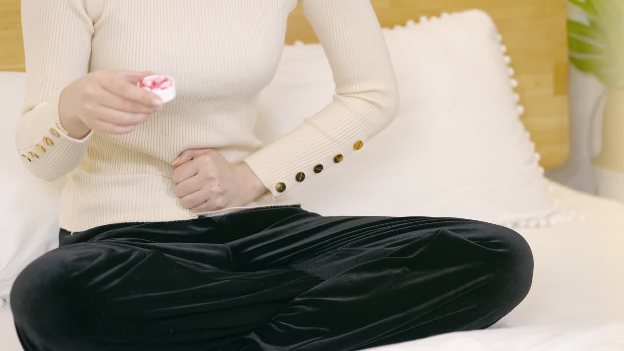 Ung kvinna med smärtor i magen, menstruationskramper och magont, grimaserar av obehag i buken, tar mediciner, kramplösande medel för att stoppa kramper och lindra matsmältningsbesvär.