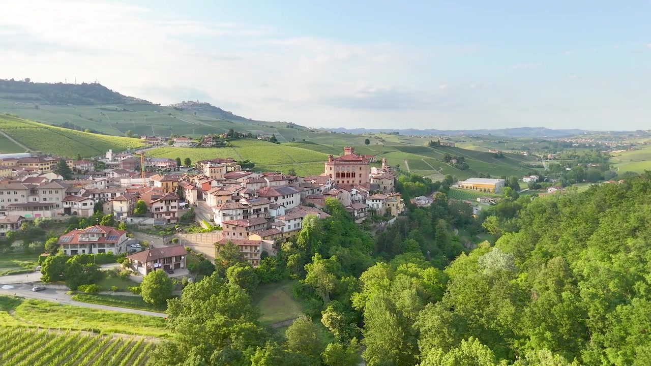 Ampia ripresa aerea di un villaggio storico italiano immerso tra dolci colline e rigogliosi vigneti