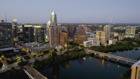 approaching lit uo skyscrapers in downtown austin, dusk in tx, usa - aerial view