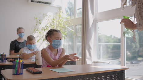 The-teacher-treats-the-hands-of-an-antiseptic-girl-in-the-classroom-at-school-before-class.-coronavirus-and-the-pandemic-at-school.-The-work-of-the-school-in-the-epidemic-mode