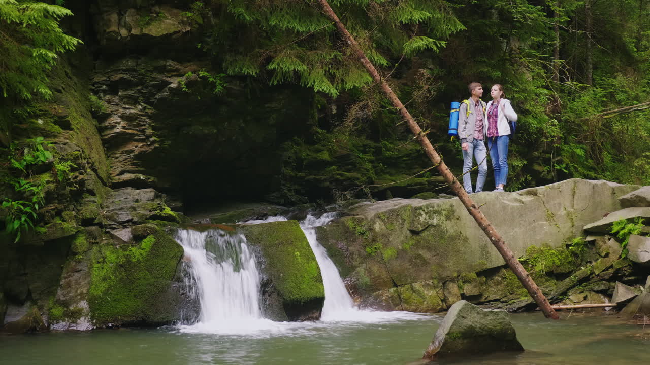 관광객의 젊은 부부는 아름다운 sc 감탄 산 강에 폭포 근처에 서있다